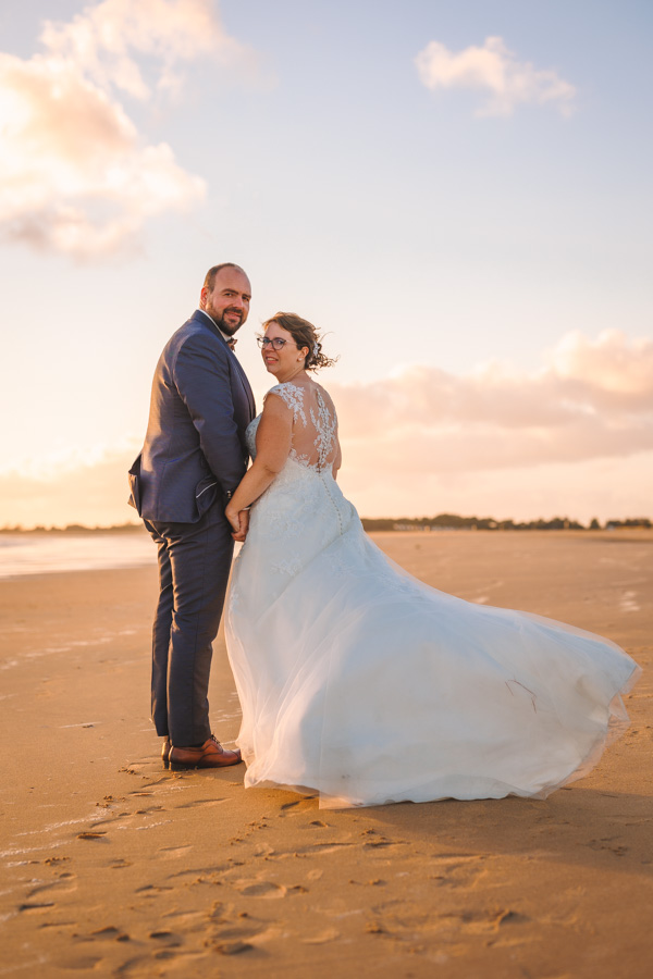Les mariés se tiennent par la main sur la plage pour les photos de leur photographe de mariage en Vendée