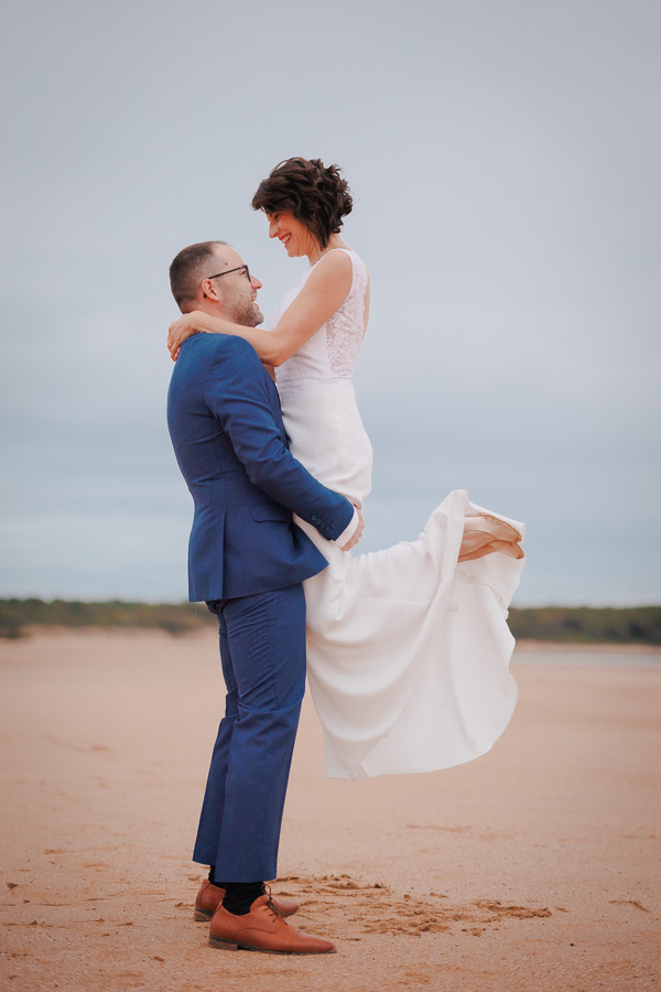 Photographie d'un photographe de mariage montrant un marié qui porte la mariée sur une plage de Vendée